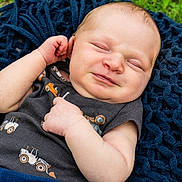 Dale is registered to the contest to win money with this photo: baby, infant, smile, face, arm, clothing, blanket, outdoor, grass, knitwear, blue, cute, child, person, portrait, sleeveless_shirt, skin, expression, relaxation, lying_down
