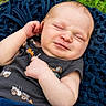 baby, infant, smile, face, arm, clothing, blanket, outdoor, grass, knitwear, blue, cute, child, person, portrait, sleeveless_shirt, skin, expression, relaxation, lying_down