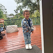 Truth joined the competition — help win amazing prizes! child, boy, smiling, plaid_shirt, jeans, white_sneakers, outdoor, deck, wooden_floor, rain, wet_surface, greenery, trees, string_lights, fence, casual_clothing, happy, standing, daylight, person