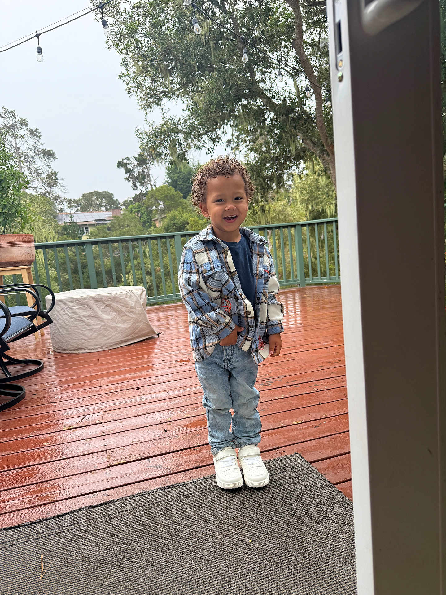 Truth joined the competition — help win amazing prizes! child, boy, smiling, plaid_shirt, jeans, white_sneakers, outdoor, deck, wooden_floor, rain, wet_surface, greenery, trees, string_lights, fence, casual_clothing, happy, standing, daylight, person
