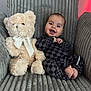 baby, teddy_bear, plush_toy, armchair, checkered_clothing, smiling, happy, infant, cute, cozy, indoor, child, soft_texture, ribbon, portrait, seated, feet, face, furniture, decor