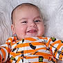 Ares is registered to the contest to win money with this photo: baby, smiling, infant, face, cute, onesie, orange, white, striped_clothing, ghost, skeleton, halloween_theme, tongue_out, soft_blanket, fluffy, close_up, child, happy, portrait, lying_down