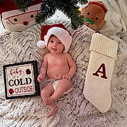 Amelia is registered to the contest to win money with this photo: baby, santa_hat, blanket, stocking, pillows, christmas_tree, holiday, festive, diaper, cute, smiling, indoor, cozy, sign, red, white, green, plush, decor, child
