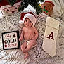 baby, blanket, child, christmas_tree, cozy, cute, decor, diaper, festive, green, holiday, indoor, pillows, plush, red, santa_hat, sign, smiling, stocking, white