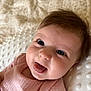 baby, blanket, child, close_up, cute, eyes, face, hair, happy, indoors, infant, lying_down, person, pink_clothing, portrait, skin, smiling, soft_light, texture, tongue_out