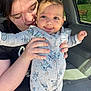 baby, woman, child, car_interior, onesie, tattoo, smiling, holding, sunlight, cute, stitch_pattern, portrait, happy, person, indoor, seat, clothing, face, hand, toddler