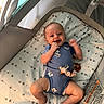 Cienna is registered to the contest to win money with this photo: baby, infant, child, smiling, happy, portrait, lying_down, bassinet, crib, blanket, stars, blue_outfit, floral_clothing, pacifier, hand_to_mouth, raised_arm, indoor, nursery, sleeping_area, newborn