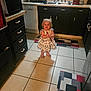 appliance, black_cabinets, blonde_hair, child, countertop, dish_rack, dishwasher, floor_mat, footwear, happy, indoors, kitchen, mat, person, sink, smiling, tile_floor, toddler, white_dress, window