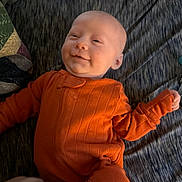 Carter joined the competition — help win amazing prizes! baby, infant, smile, orange_clothing, blanket, lying_down, hand, cozy, child, cute, indoors, portrait, soft_light, young_child, sleepwear, human, face, skin, expression, comfort