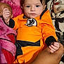 Anthony is registered to the contest to win money with this photo: baby, child, orange_clothing, hand, blanket, bed, patterned_bedding, person, infant, holding_hands, cute, portrait, indoors, soft_texture, sleepwear, young_child, comfort, resting, close_up, human