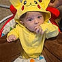 Anthony is registered to the contest to win money with this photo: baby, child, pikachu_onesie, yellow_clothing, hood, ears, baby_seat, blanket, hand, thumb_in_mouth, carpet, indoor, person, cute, infant, face, eyes, sitting, colorful, cozy
