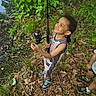 child, smiling, fishing_rod, outdoor, nature, greenery, leaves, ground, grass, tree, boy, shorts, sneakers, happy, playful, summer, adventure, people, toy, forest