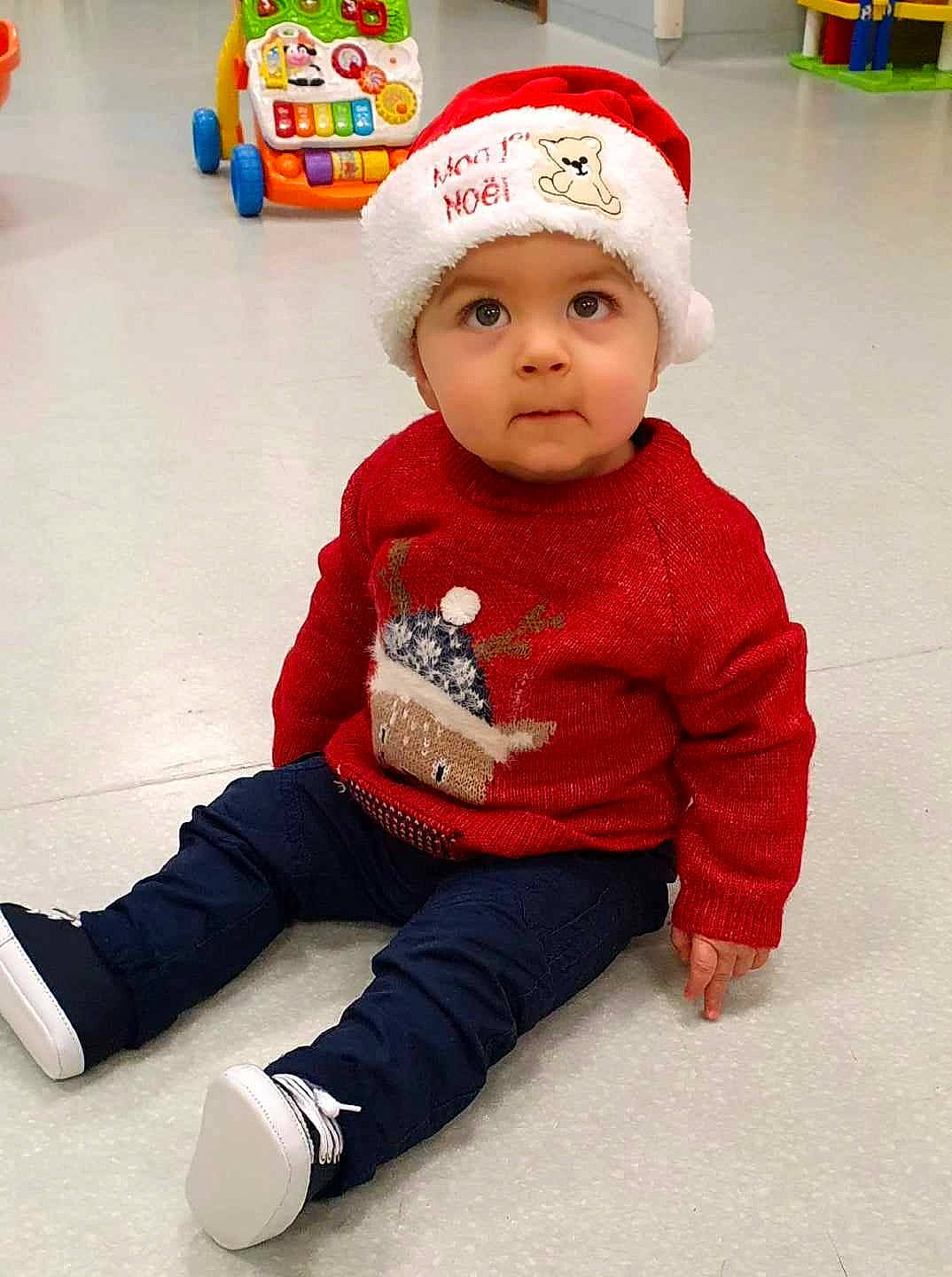 Diego a rejoint le concours — aidez-le/la à gagner de superbes lots ! baby, baby_toddler_clothing, beanie, cap, child, flooring, fun, headgear, headwear, jacket, knit_cap, leg, leisure, outerwear, pattern, person, sitting, sleeve, t_shirt, toddler