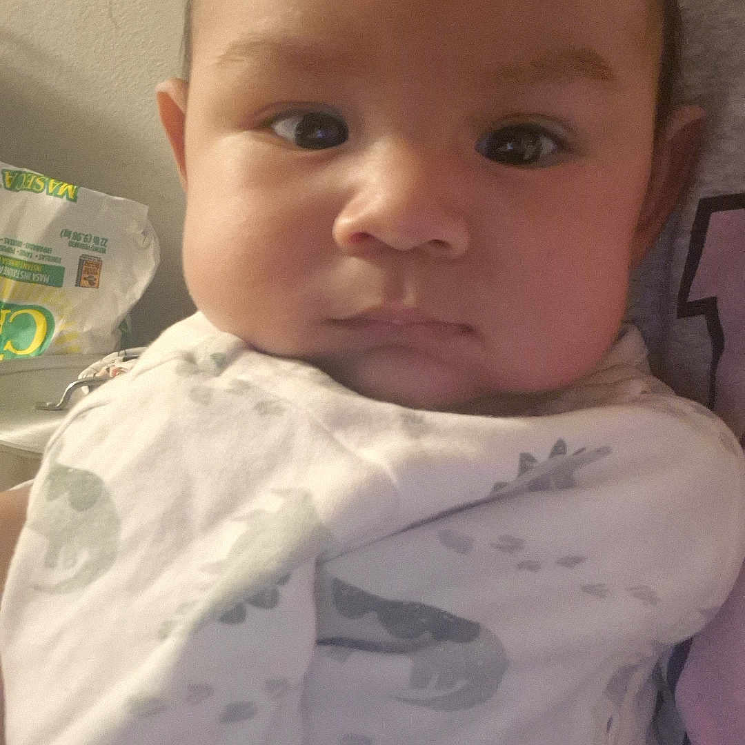 Steven joined the competition — help win amazing prizes! baby, infant, child, portrait, close_up, face, serious, indoors, blanket, dinosaur_pattern, clothing, pillow, couch, seated, looking_at_camera, brown_hair, eyes, home, cozy, photography