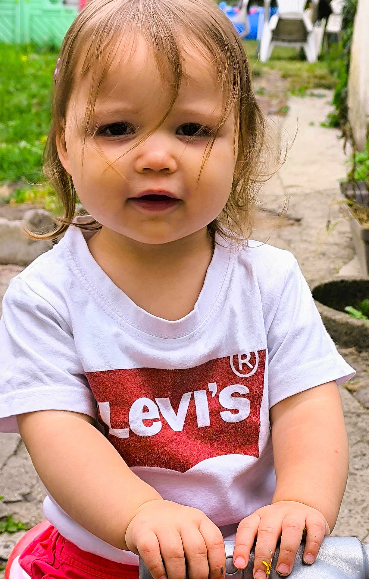 Lola participe au concours pour gagner de l'argent avec cette photo : toddler, child, outdoor, grass, garden, tshirt, white_clothing, red_shorts, hands, face, hair, curly_hair, smiling, person, playground, toy, nature, daylight, young_child, casual_clothing