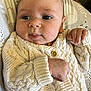 baby, infant, knitted_sweater, cream_color, wooden_buttons, close_up, face, hand, cushion, patterned_background, cute, portrait, child, young, cozy, indoor, soft_light, looking, expression, newborn