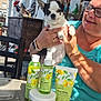 dog, person, skincare_products, table, outdoor, balcony, glass_table, bottle, tube, jar, lemon, decor, rooster_statue, woman, glasses, smile, hand, sunlight, casual_clothing, pet