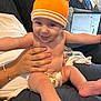 Louie joined the competition — help win amazing prizes! baby, smiling, orange_hat, diaper, hand, couch, blanket, laptop, indoor, person, happy, child, skin, blue_eyes, casual, home, technology, seated, holding, clothing