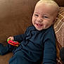 baby, smiling, toy, couch, blue_clothing, infant, happy, child, indoor, person, plush, seat, cute, young_child, relaxed, head, face, hand, sitting, cozy