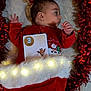 Raphaël a rejoint le concours — aidez-le/la à gagner de superbes lots ! baby, infant, christmas, holiday, stocking, lights, red_clothing, tinsel, milestone_card, face, side_profile, cute, festive, soft_texture, blanket, lying_down, child, celebration, indoors, adorable