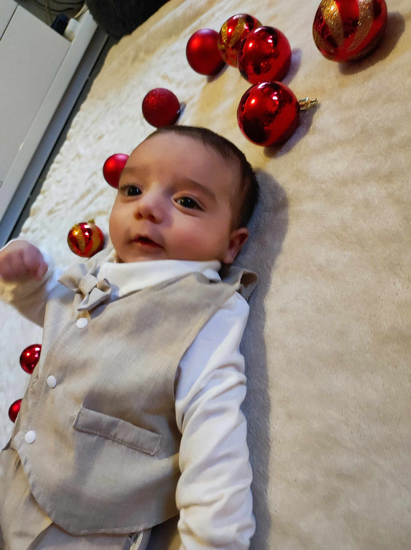 Raphaël a rejoint le concours — aidez-le/la à gagner de superbes lots ! baby, infant, child, vest, white_shirt, red_ornaments, christmas_decor, blanket, laying_down, holiday, cute, face, portrait, indoor, soft_texture, festive, smile, young_child, holiday_decor, celebration