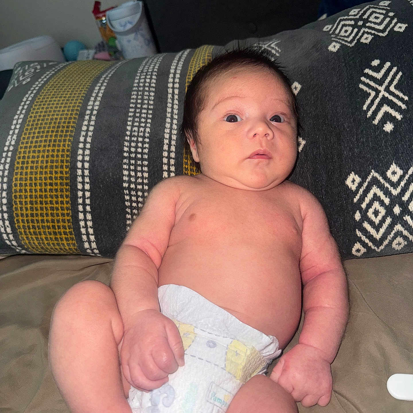 Ryker is registered to the contest to win money with this photo: newborn, baby, infant, child, portrait, sitting, diaper, wide_eyed, face, skin, couch, cushion, blanket, home, indoors, patterned_fabric, photography, close_up, head, body
