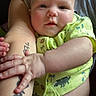 arm, baby, child, closeup, comfort, cute, expression, face, hand, holding, human, indoors, infant, person, portrait, sitting, skin, tattoo, yellow_clothing, young