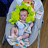 baby, infant, child, bouncer, plush_toy, green_toy, sitting, indoor, portrait, face, eyes, clothing, socks, baby_bottle, colorful, blanket, wooden_floor, furniture, cozy, photograph