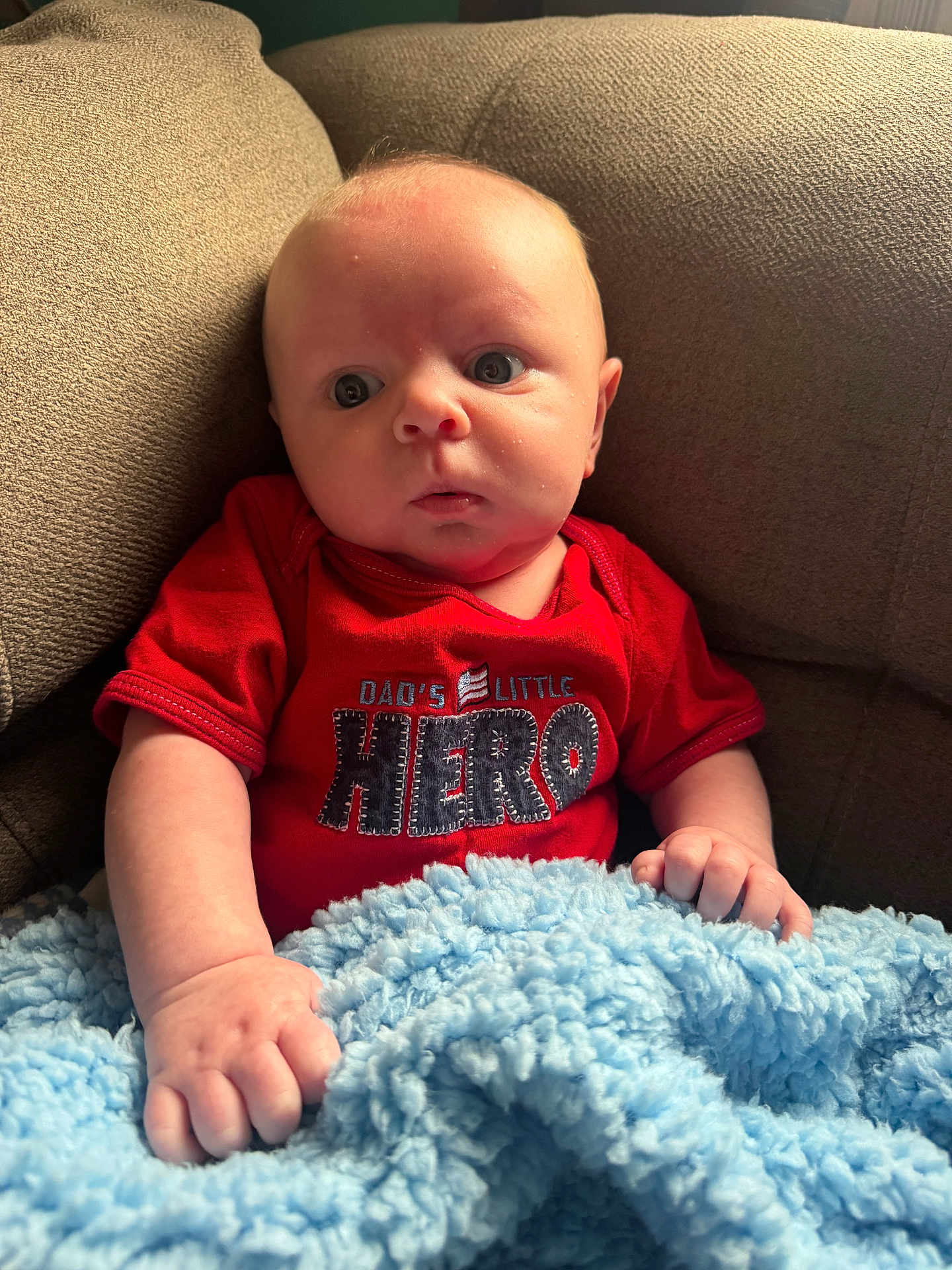 Jason joined the competition — help win amazing prizes! baby, infant, red_shirt, blanket, blue_blanket, couch, furniture, indoors, child, person, cute, face, skin, hand, seated, expression, young, portrait, clothing, cozy