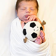 Zozo a rejoint le concours — aidez-le/la à gagner de superbes lots ! newborn, baby, sleeping, wrapped, blanket, plush_toy, soccer_ball, soft, cute, peaceful, infant, feet, hand, face, portrait, white_background, child, resting, cozy, adorable