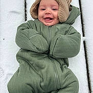 Zakari joined the competition — help win amazing prizes! baby, smiling, snow, green_snowsuit, knitted_hat, winter_clothing, outdoor, cold_weather, wooden_surface, face, happy, infant, cute, child, cozy, warm_clothing, portrait, person, winter, fun