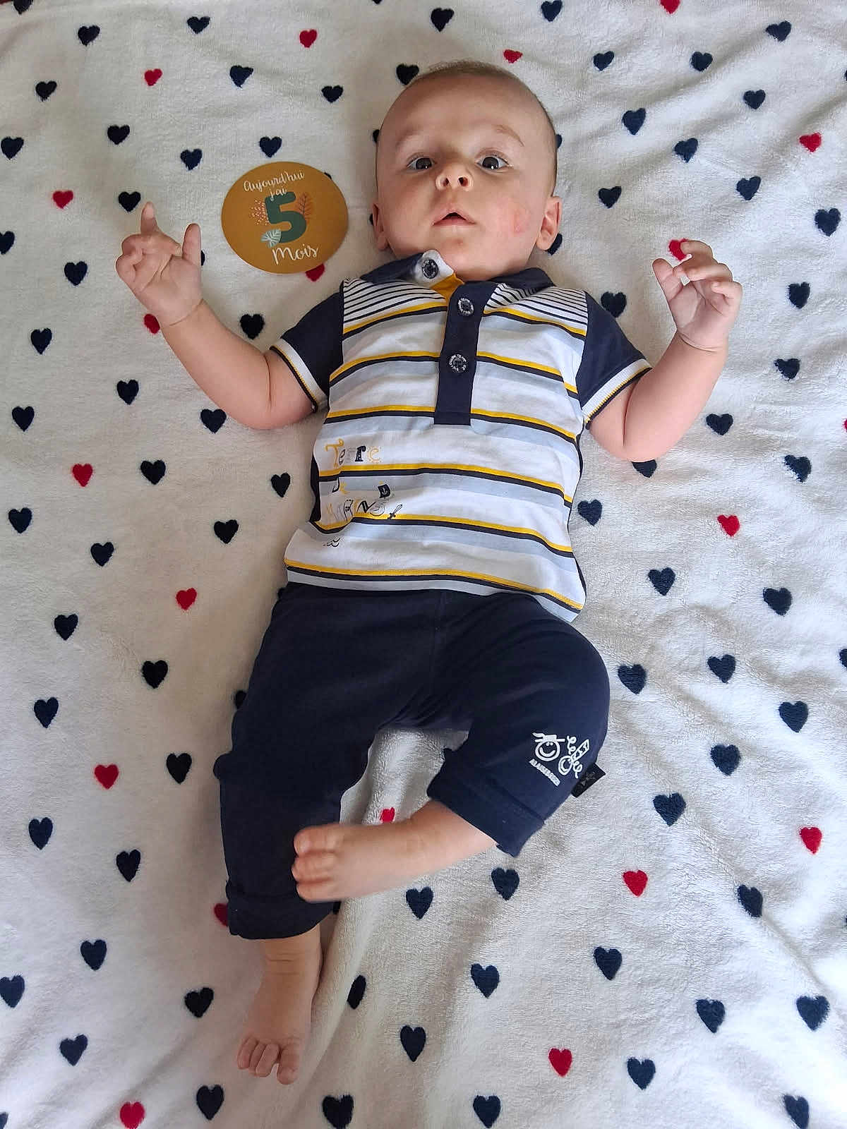 Malo a rejoint le concours — aidez-le/la à gagner de superbes lots ! baby, infant, child, lying_down, striped_shirt, navy_pants, blanket, heart_pattern, sign, 5_months, cute, hand_gesture, curious, relaxed, indoors, portrait, young_child, clothing, foot, face