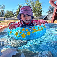 Waylyn is registered to the contest to win money with this photo: toddler, child, pool, water, inflatable_ring, hat, swimsuit, summer, outdoor, happy, splash, sunny, backyard, blue_sky, trees, play, person, recreation, fun, daytime