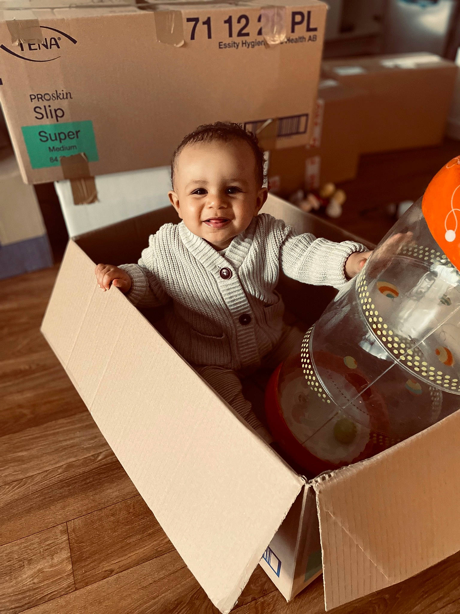 Owen a rejoint le concours — aidez-le/la à gagner de superbes lots ! baby, baby_toddler_clothing, box, cardboard, carton, child, flooring, happy, hardwood, joy, packaging_and_labeling, packing_materials, paper_product, person, rectangle, room, shipping_box, sleeve, smile, t_shirt