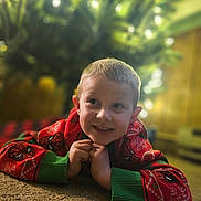 Everett is registered to the contest to win money with this photo: child, boy, smiling, lying_down, carpet, christmas_tree, holiday_sweater, red_sweater, green_cuffs, spiderman, indoors, holiday, festive, portrait, happy, blurred_background, warm_lighting, young_child, cute, casual