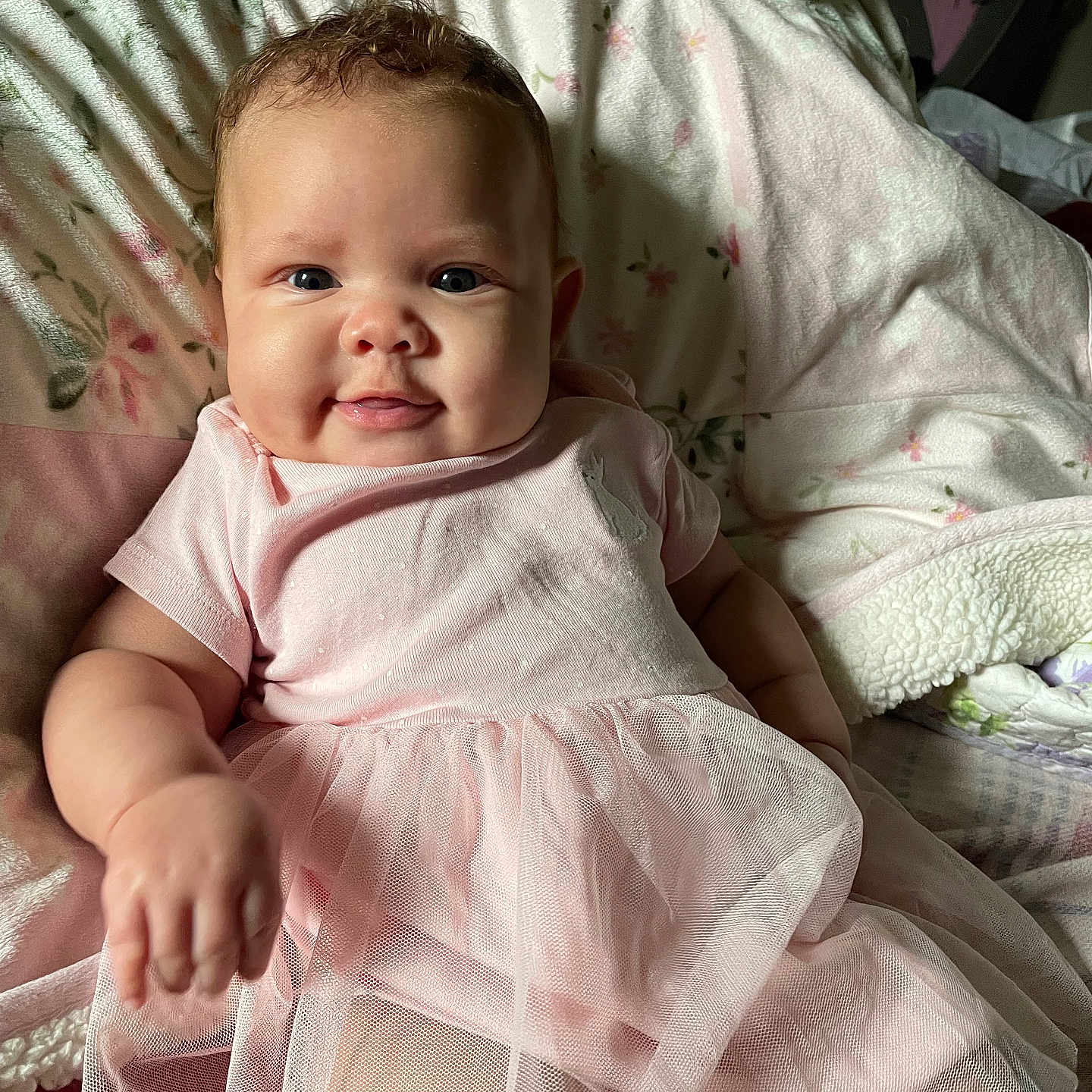 Ember is registered to the contest to win money with this photo: adorable, baby, blanket, candid, cheerful, child, closeup, cozy, cute, floral_pattern, happy, indoors, infant, pink_dress, portrait, relaxing, smile, soft_lighting, tulle_skirt, young_child