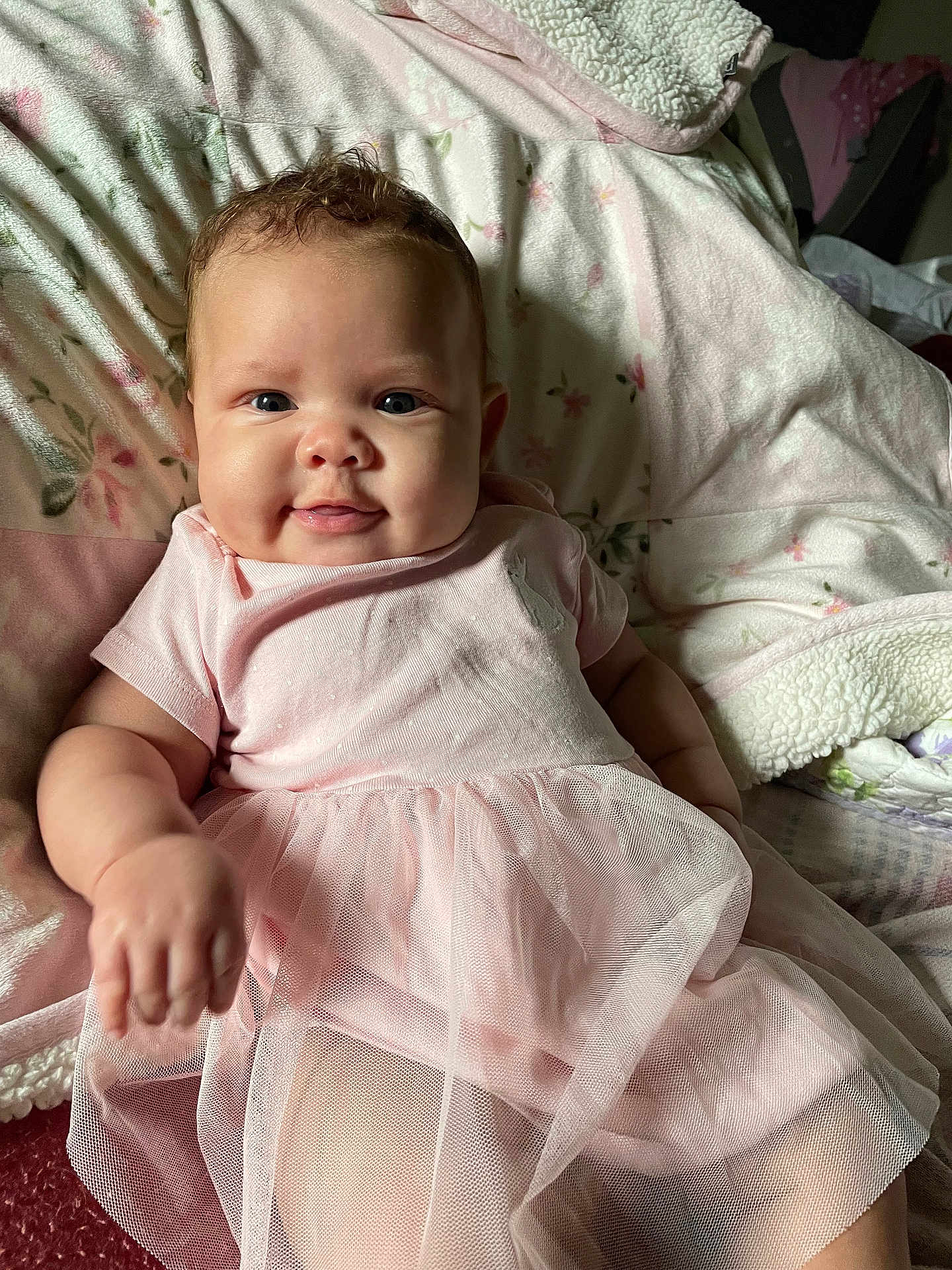 Ember is registered to the contest to win money with this photo: baby, infant, smile, pink_dress, blanket, cozy, cute, child, portrait, indoors, happy, soft_lighting, closeup, candid, tulle_skirt, young_child, relaxing, floral_pattern, cheerful, adorable