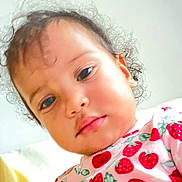Eva is registered to the contest to win money with this photo: child, curly_hair, face, portrait, closeup, strawberry_pattern, shirt, young_child, casual_clothing, indoors, soft_lighting, calm_expression, person, cute, baby, earrings, pink, red, green, skin