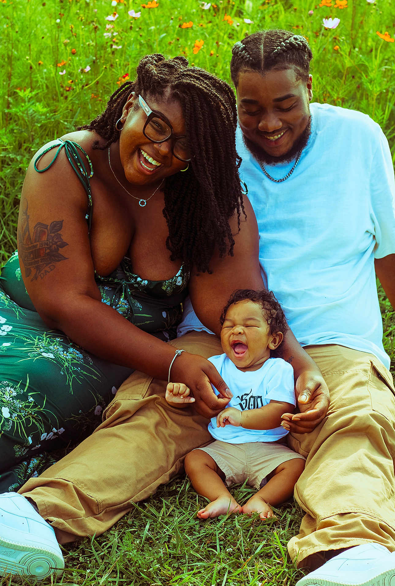 Adrian joined the competition — help win amazing prizes! baby, smiling, family, outdoor, grass, wildflowers, happy, sitting, adult, person, casual_clothing, glasses, tattoo, green_dress, shorts, white_shirt, barefoot, joy, nature, portrait