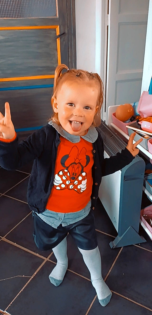 Lia participe au concours pour gagner de l'argent avec cette photo : baby, baby_toddler_clothing, child, finger, flooring, fun, gesture, hairstyle, happy, human_body, joint, leg, orange, person, product, shorts, sleeve, smile, standing, thumb