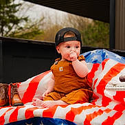Lorenzo is registered to the contest to win money with this photo: baby, child, cap, overalls, american_flag, blanket, cowboy_boots, cake, birthday_candle, outdoor, truck_bed, celebration, half_birthday, cute, sitting, footwear, person, hat, plaid, nature
