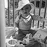 baby, child, hat, toy, blanket, sitting, outdoor, fence, shirt, sweater, mirror, car_toy, plush_toy, grass, sunlight, portrait, cute, infant, black_and_white, expression