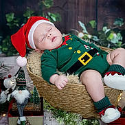 Elijah Finn joined the competition — help win amazing prizes! baby, sleeping, christmas, santa_hat, elf_outfit, basket, decorations, lantern, gnome, fairy_lights, holiday, festive, cozy, wood_floor, plush, greenery, red_shoes, indoors, cute, seasonal