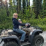 adult, baby, atv, all_terrain_vehicle, forest, outdoors, evergreen_trees, nature, sunlight, family, parent, infant, vehicle, motorized_vehicle, off_road, gravel, smiling, sunglasses, protective_clothing, adventure
