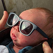 Xander is registered to the contest to win money with this photo: newborn, baby, infant, sunglasses, portrait, close_up, face, sleeping, clothing, jacket, blanket, adult_hand, indoor, candid, fashion, cute, head, skin, eyewear, family