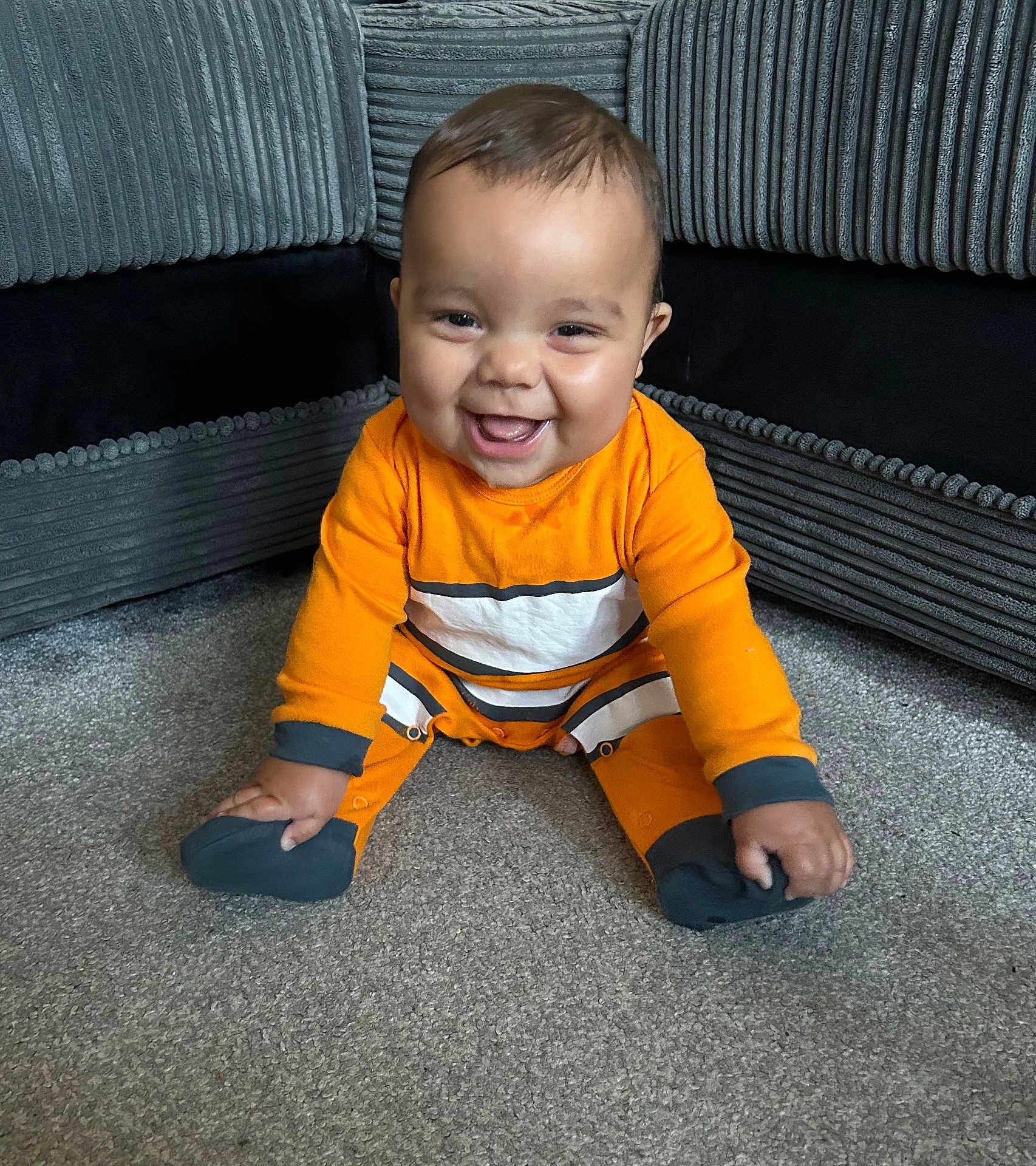 Freddie joined the competition — help win amazing prizes! baby, child, smiling, orange_clothing, sitting, carpet, indoor, furniture, sofa, happy, cute, portrait, infant, cozy, young_child, floor, person, bright_colors, home, comfort