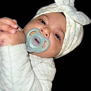 Jimma is registered to the contest to win money with this photo: adorable, baby, black_background, bow, child, closeup, cute, expression, face, hand, headwrap, infant, looking, newborn, pacifier, portrait, quilted, skin, soft, white_clothing