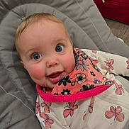 Paisley is registered to the contest to win money with this photo: baby, child, face, blue_eyes, smile, bib, butterfly_pattern, floral, clothing, cushion, seat, happy, infant, indoors, person, cute, cheeks, apparel, fabric, closeup