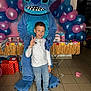 Zaïm participe au concours pour gagner de l'argent avec cette photo : child, boy, costume, stitch, balloons, party, celebration, peace_sign, smile, jeans, white_shirt, sneakers, indoor, floor_tiles, gift_boxes, table, decorations, festive, portrait, fun