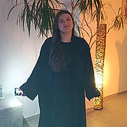 Clara a rejoint le concours — aidez-le/la à gagner de superbes lots ! indoor, person, young_adult, plant, lamp, phone, selfie, tile_floor, long_hair, black_clothing, barefoot, decor, wall, smile, standing, technology, casual, light, shadow, relaxed